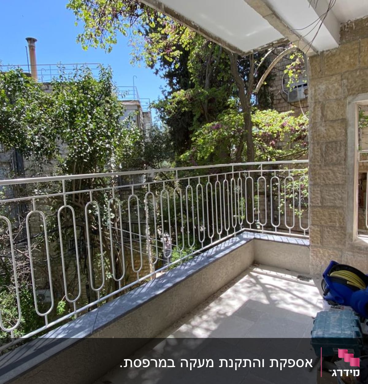 מעקה מתכת לבן במרפסת עם צמחייה ברקע